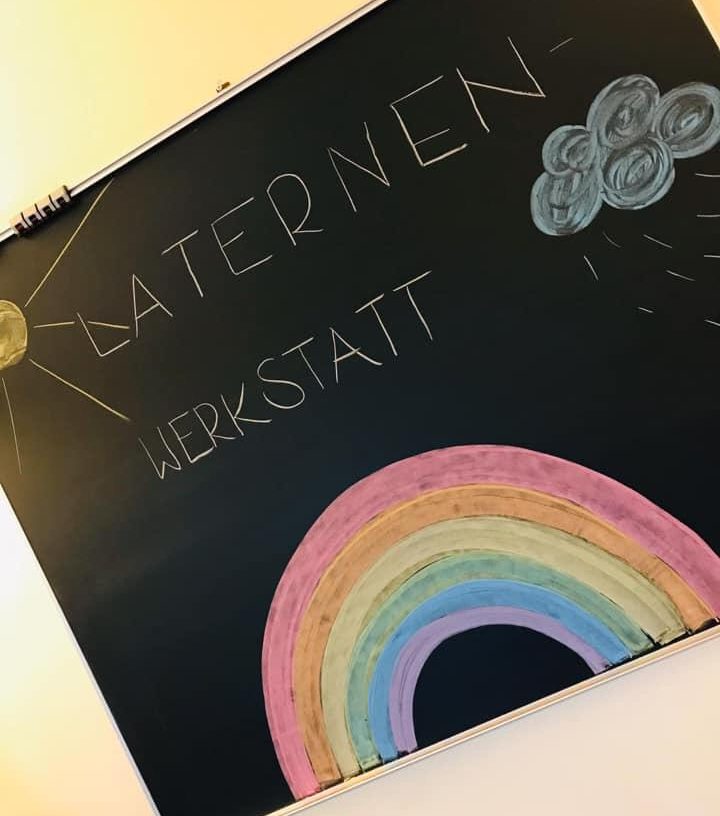 Tafel mit der Aufschrift Laternenwerkstatt und einem gemalten Regenbogen