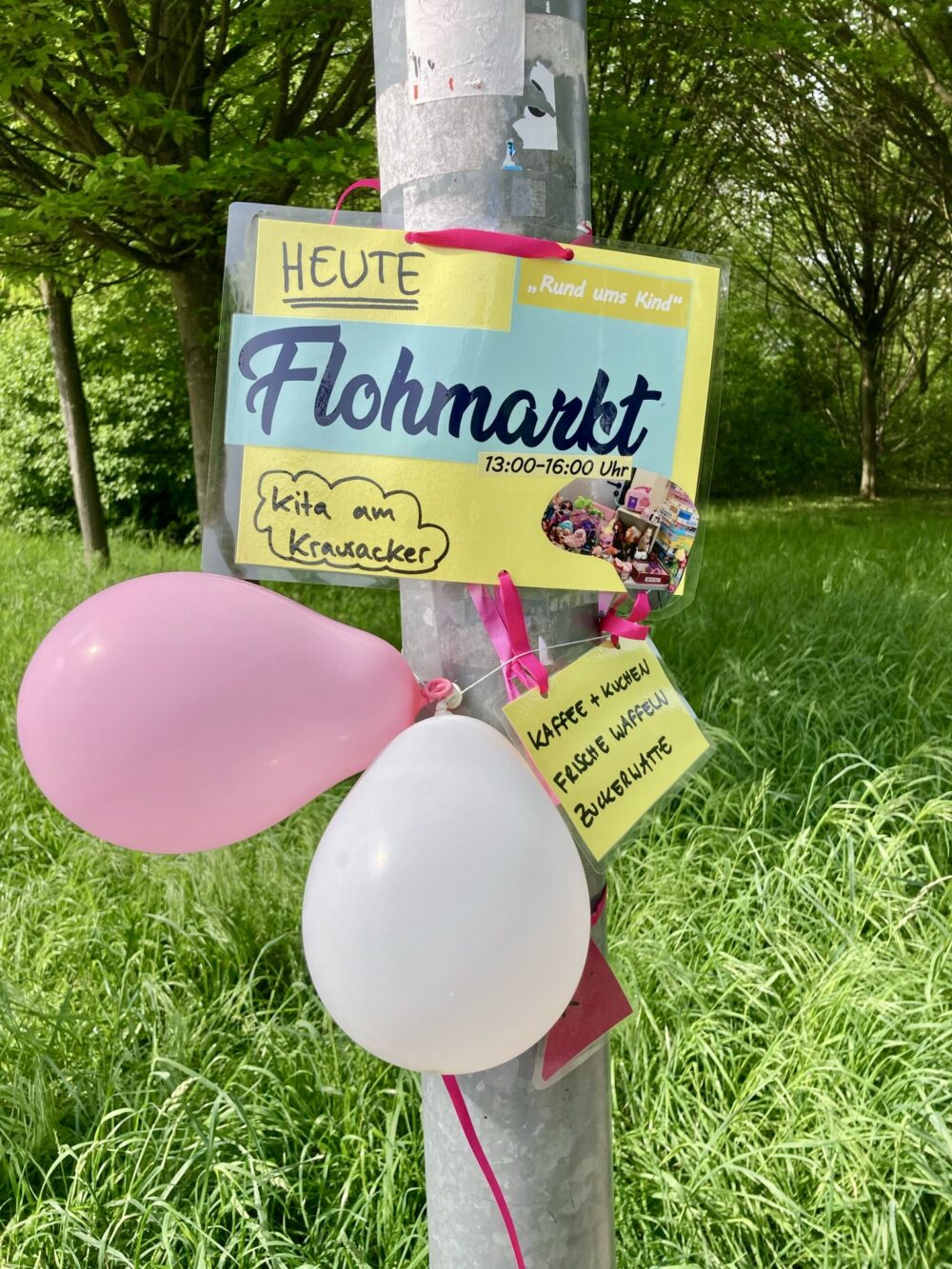 Flohmarkt-Hinweisschild mit Luftballons an einem Laternenmast