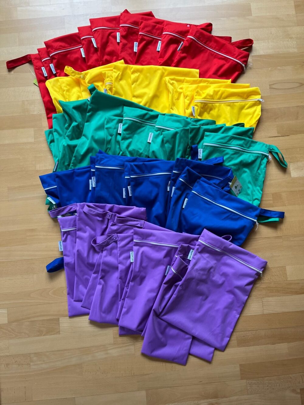 Wetbags in Rot, Gelb, Grün, Blau und Lila auf einem Holzboden