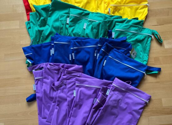 Wetbags in Rot, Gelb, Grün, Blau und Lila auf einem Holzboden