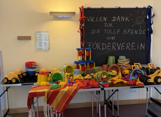 Tisch voller neuer Spielsachen vor einer Tafel mit der Aufschrift Vielen Dank für die tolle Spende vom Förderverein