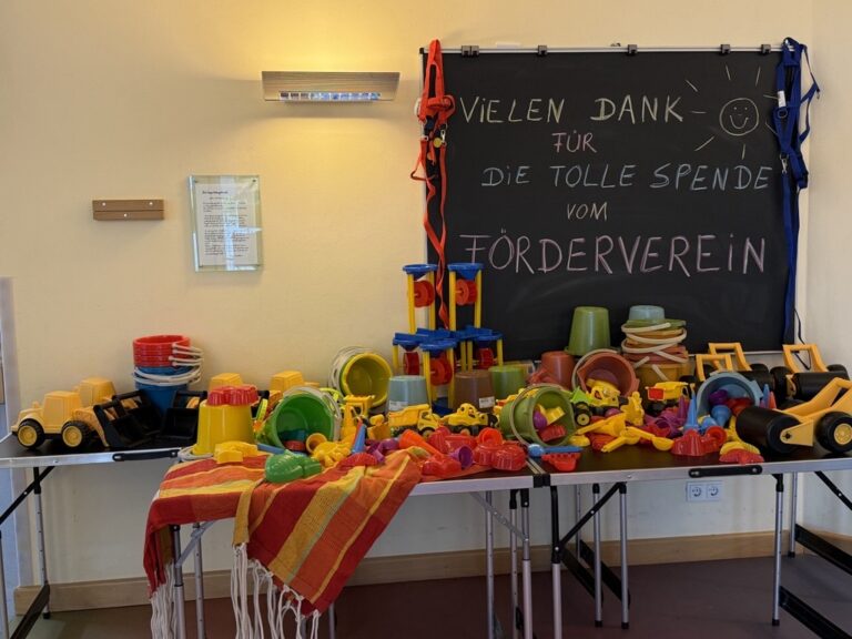 Tisch voller neuer Spielsachen vor einer Tafel mit der Aufschrift Vielen Dank für die tolle Spende vom Förderverein