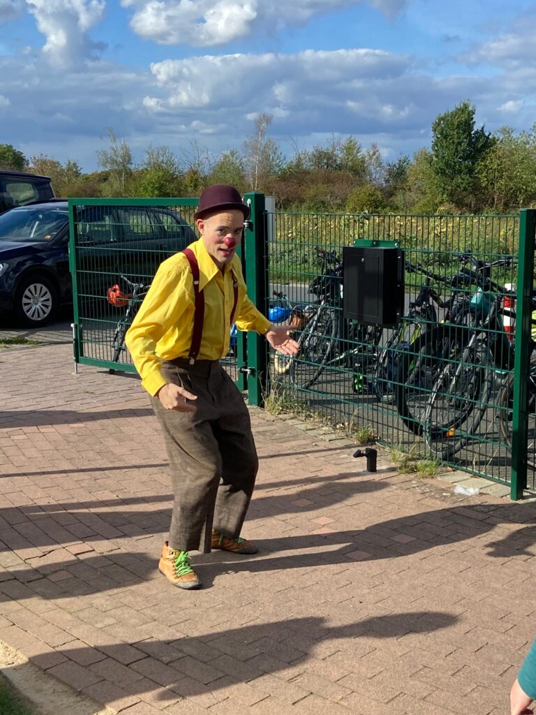 Clown Olli mit gelbem Hemd, roter Nase und Melone auf dem Kita-Gelände