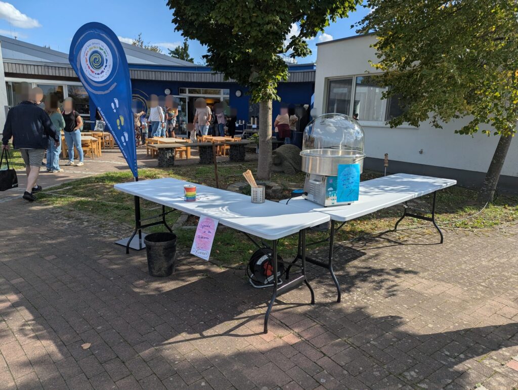 Zuckerwattestand des Fördervereins beim KiTa-Fest mit Vereinsbanner, im Hintergrund feiernde Eltern