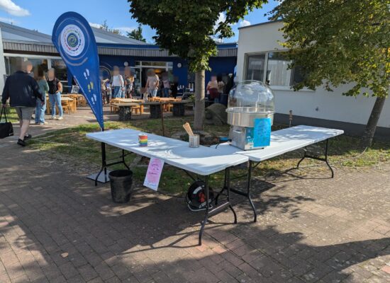 Zuckerwattestand des Fördervereins beim KiTa-Fest mit Vereinsbanner, im Hintergrund feiernde Eltern